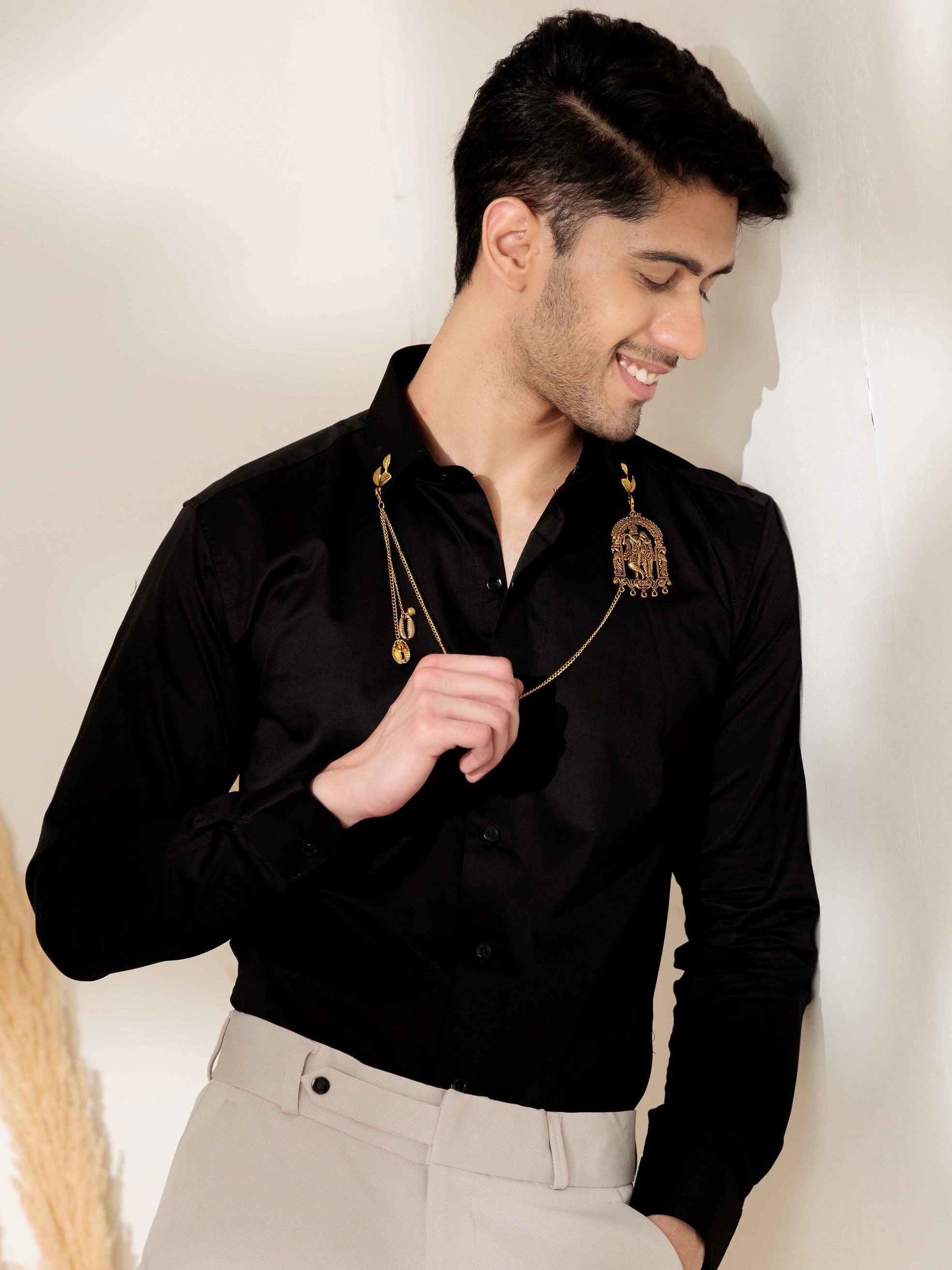 Man wearing a black shirt with gold accents against a neutral background